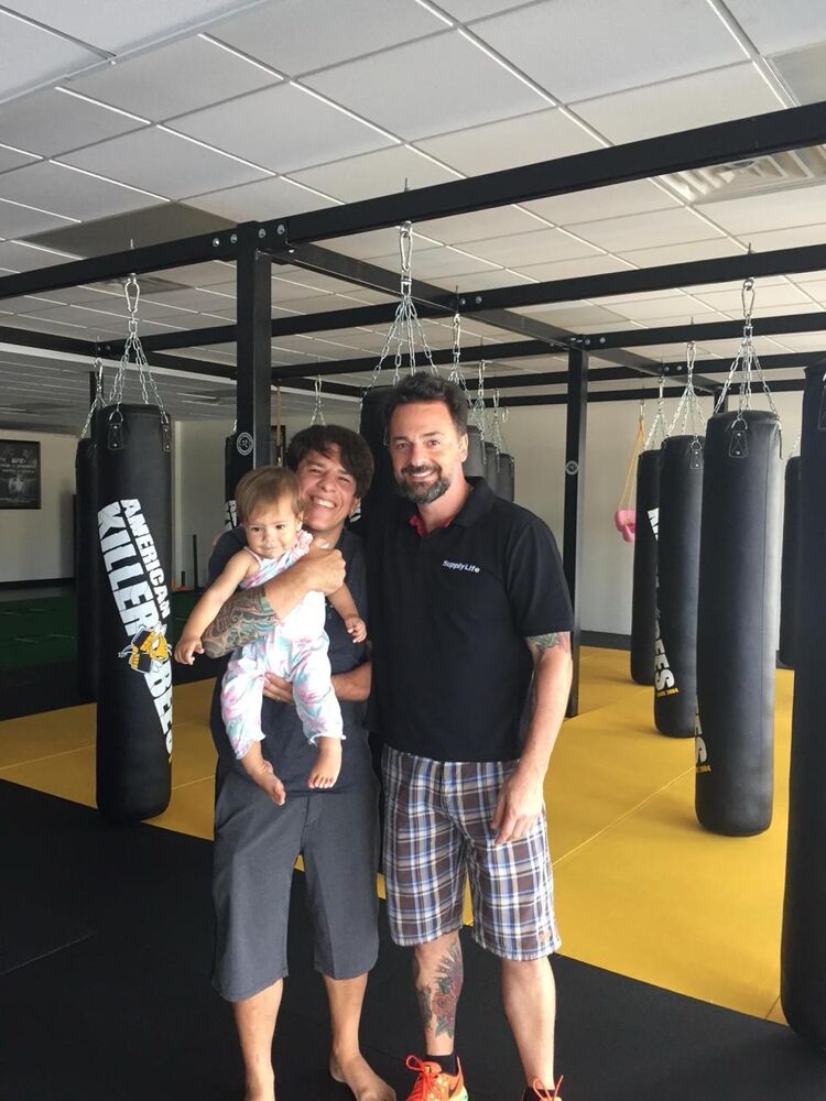 Francisco Vieira ao lado do mestre Israel Gomes, que segura a filha Valentina, numa academia de lutas