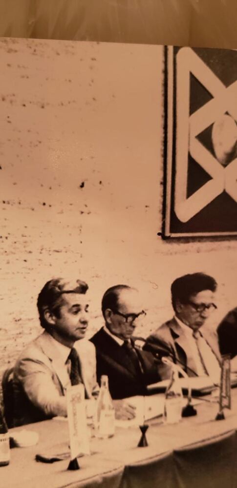 Foto antiga de uma reunião do Banco Bamerindus, com homens à mesa e o logotipo do banco ao fundo