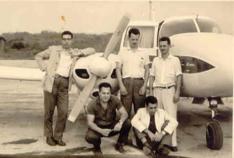 Foto antiga de cinco homens posando diante de um avião bimotor